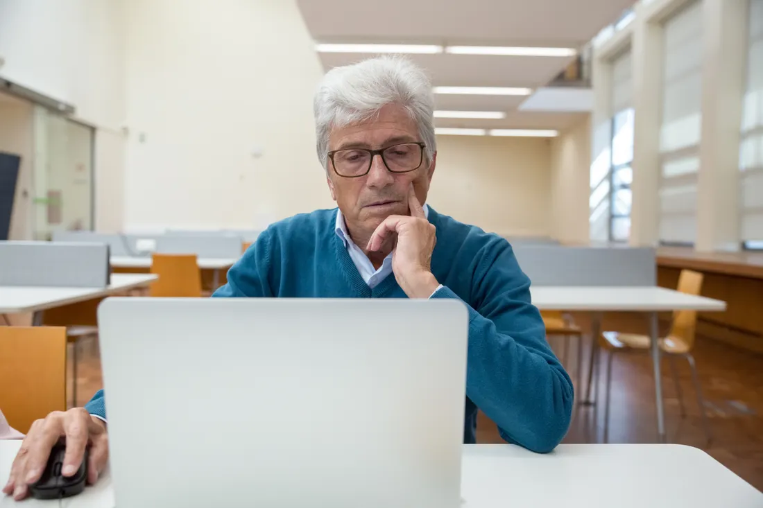 Voksen mann med briller arbeider konsentrert på en bærbar PC i et bibliotek